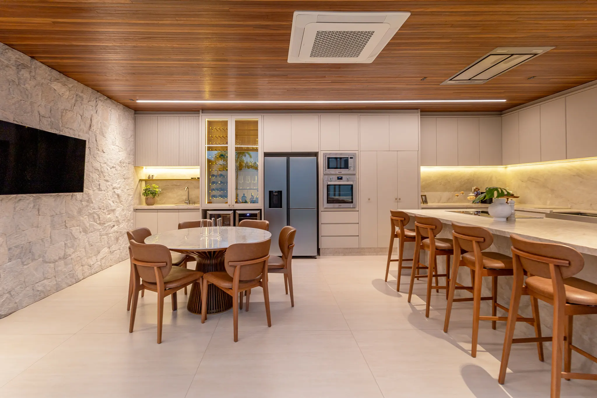 Área gourmet planejada com marcenaria em madeira, ilha de mármore e bancada com banquetas